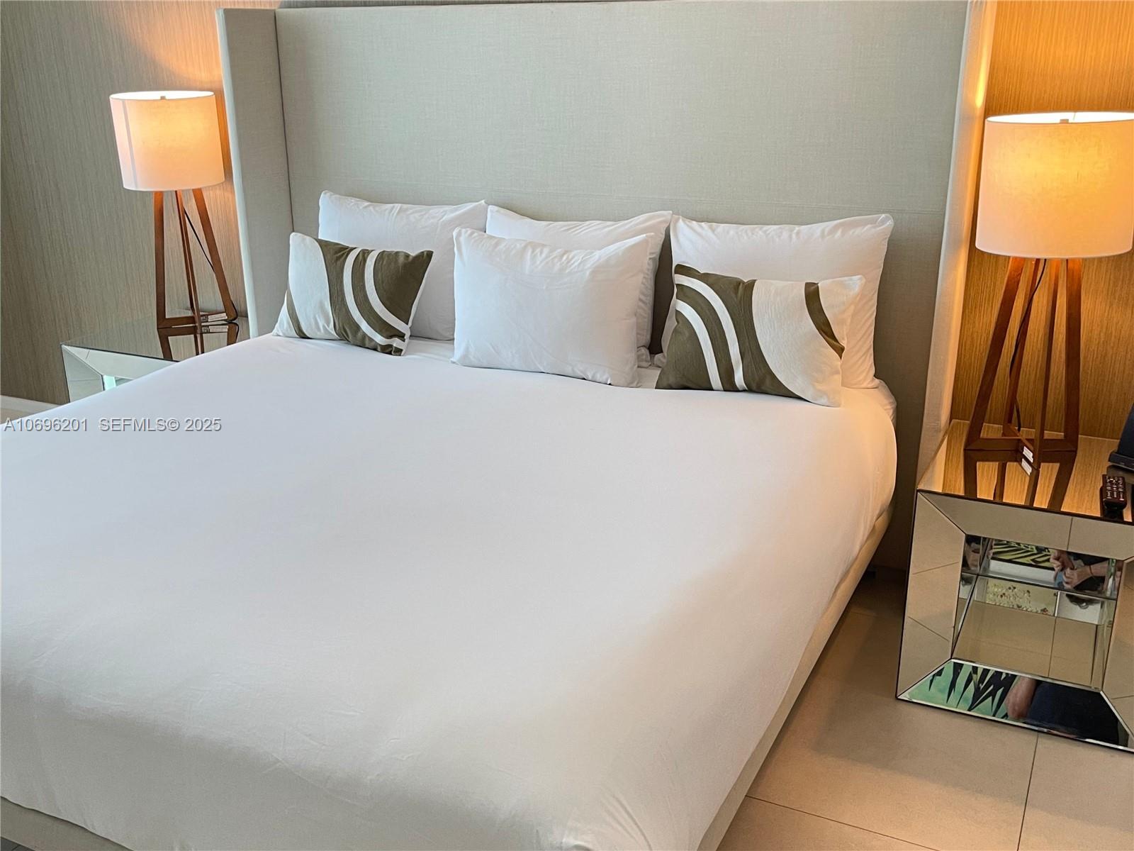 A bedroom features a bed with white linens, decorative pillows, and two wooden lamps — 4111 S OCEAN DR # 1107, Hollywood FL 33019, HOLLYWOOD, FL