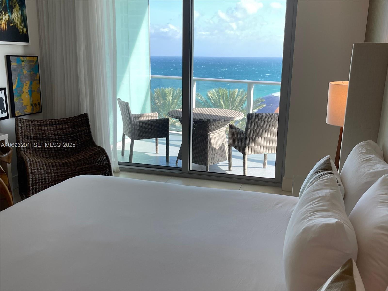 A bedroom features a bed, a wicker chair, and a balcony overlooking the ocean — 4111 S OCEAN DR # 1107, Hollywood FL 33019, HOLLYWOOD, FL
