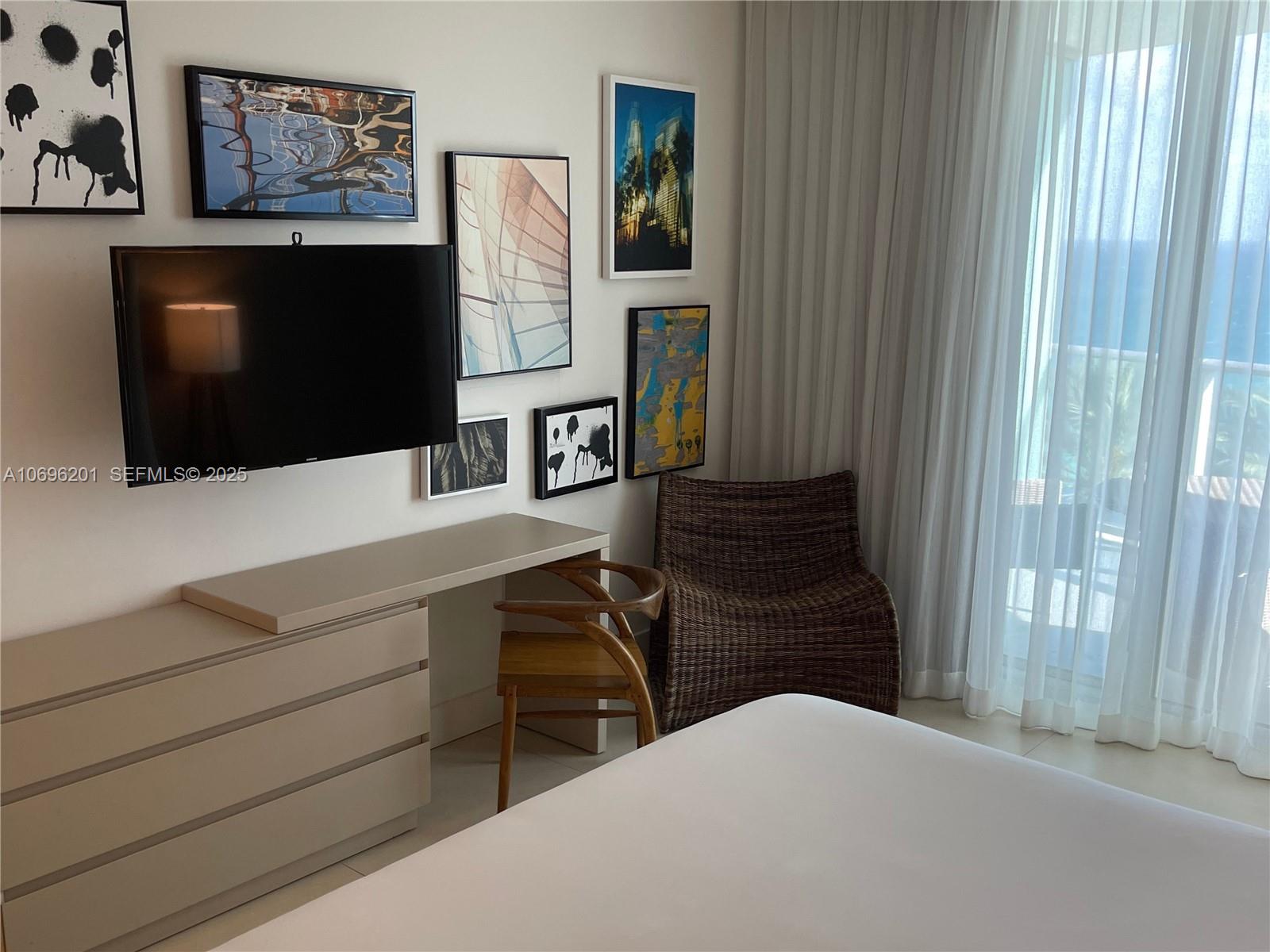 A bedroom features a wall-mounted television, a desk with a wooden chair, and a wicker chair — 4111 S OCEAN DR # 1107, Hollywood FL 33019, HOLLYWOOD, FL
