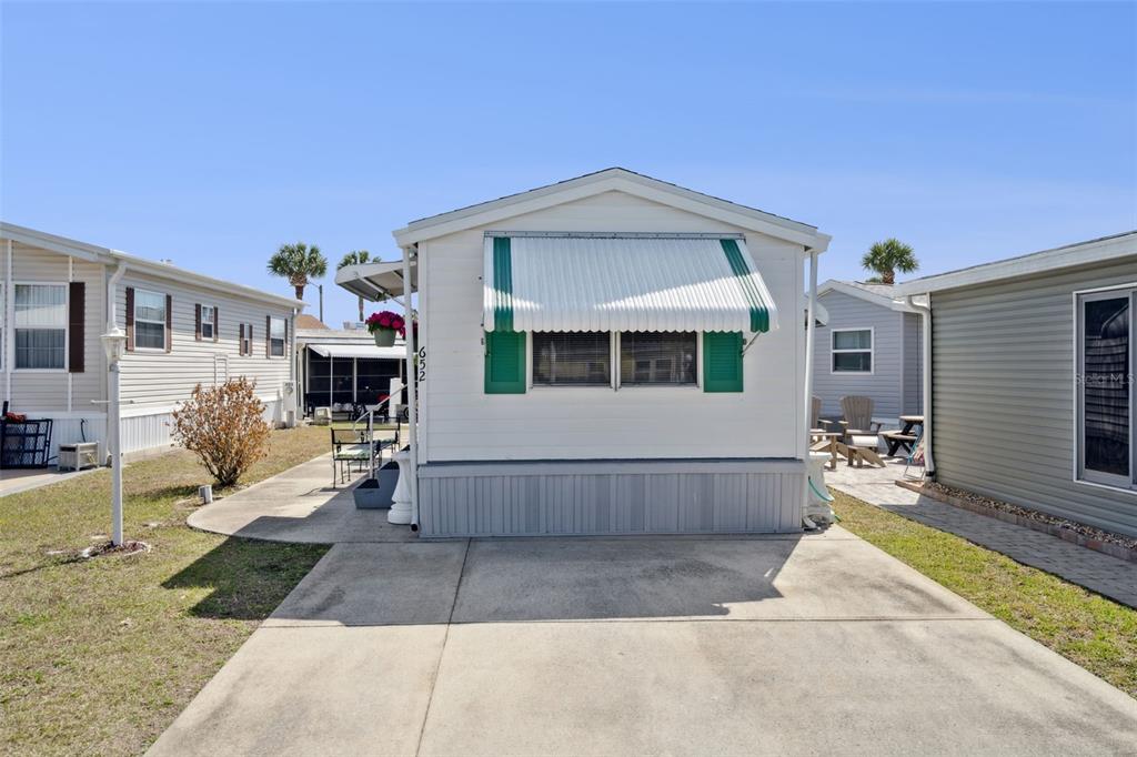 A white mobile home with green shutters and an awning sits on a concrete driveway — 9000 US HIGHYWAY 192 UNIT 652, CLERMONT, FL