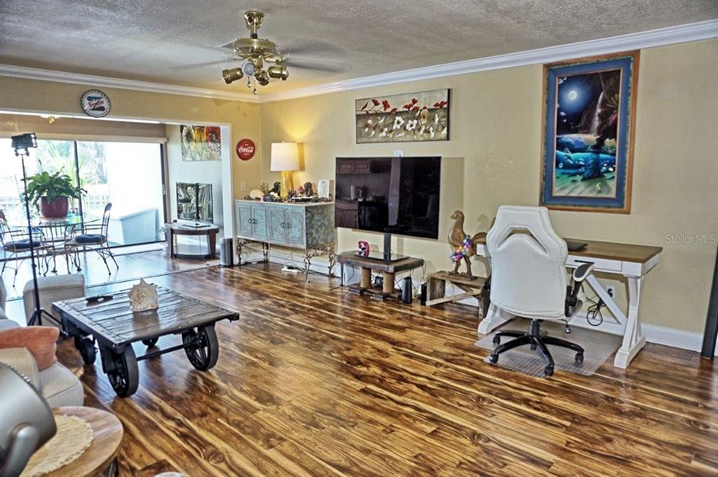 A living room features wood-look flooring, a ceiling fan, a television, and a desk area — 1873 MAZO MANOR UNIT 5, LUTZ, FL