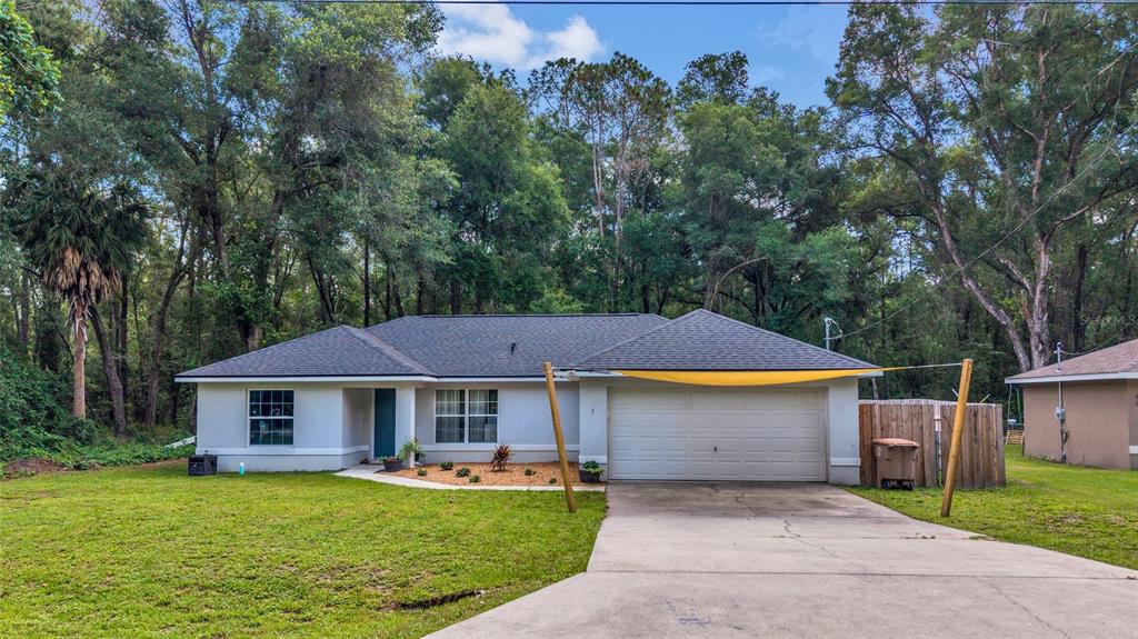 A single-story house with a gray roof, white exterior, and a driveway with a shade sail — 9 SEQUOIA LOOP LANE, OCKLAWAHA, FL
