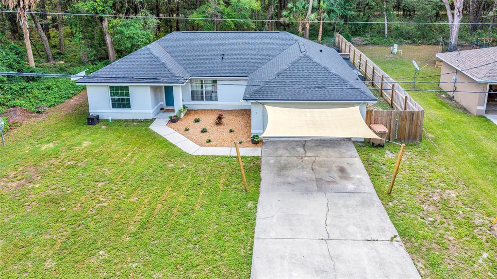 An aerial view shows a single-story house with a dark roof, driveway, and shade sail — 9 SEQUOIA LOOP LANE, OCKLAWAHA, FL