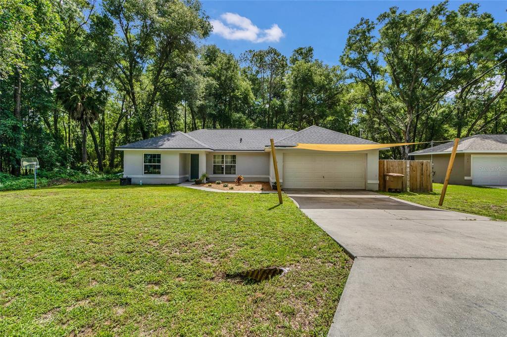 A single-story house with a two-car garage and a yellow shade sail in the driveway — 9 SEQUOIA LOOP LANE, OCKLAWAHA, FL