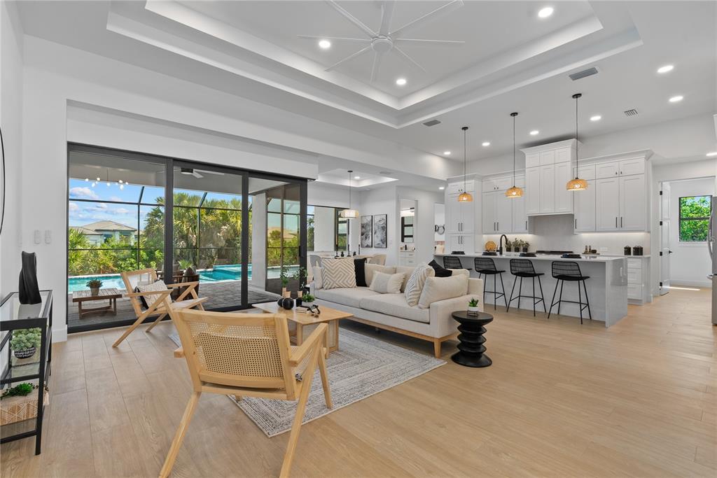 An open-concept living room and kitchen feature light wood floors, white cabinetry, and sliding glass doors — 15101 LEIPZIG CIRCLE, PORT CHARLOTTE, FL