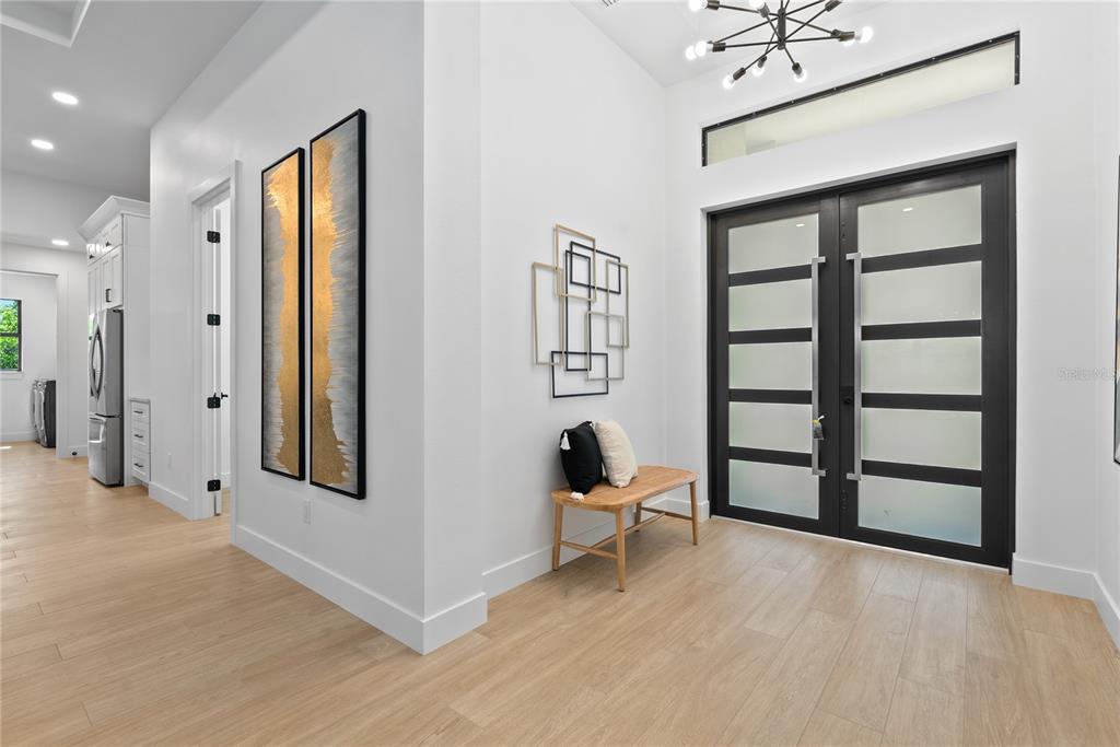 A modern entryway features light wood floors, a wooden bench, and double glass-paneled doors — 15101 LEIPZIG CIRCLE, PORT CHARLOTTE, FL