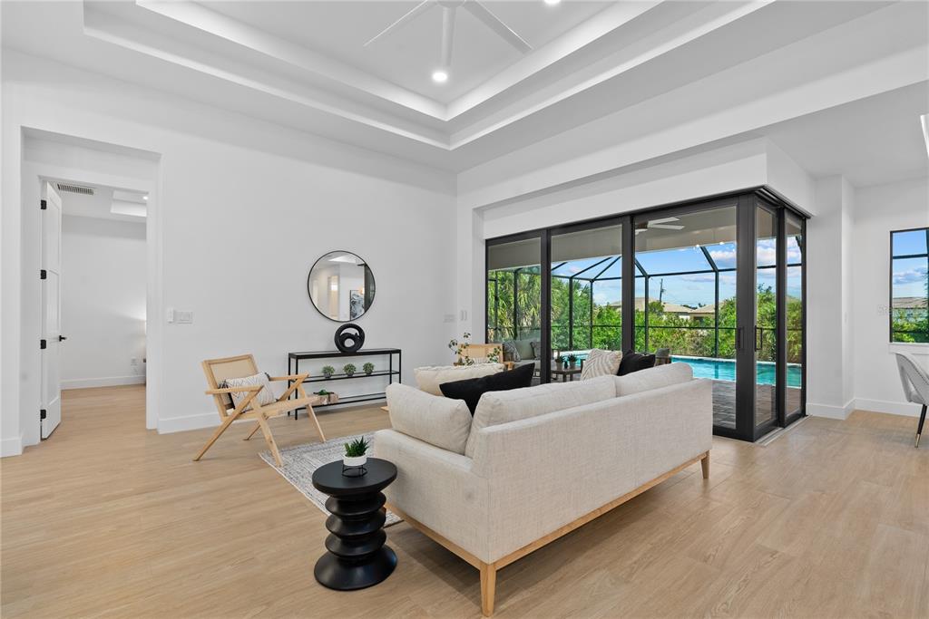 A living room features a tray ceiling, light wood flooring, and sliding doors opening to a pool — 15101 LEIPZIG CIRCLE, PORT CHARLOTTE, FL