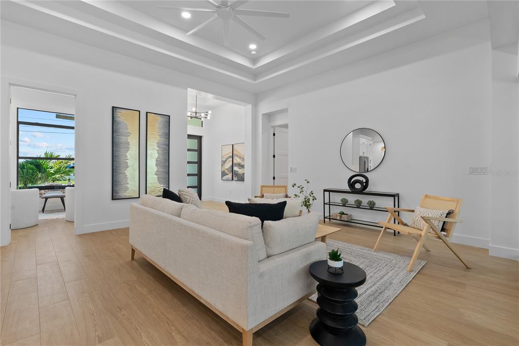 A bright living room features a tray ceiling, light wood floors, and modern minimalist decor — 15101 LEIPZIG CIRCLE, PORT CHARLOTTE, FL