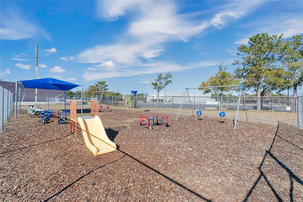 A fenced outdoor playground features a slide, swing set, and various play equipment on mulch — 7429 WEST COLONIAL DRIVE, ORLANDO, FL