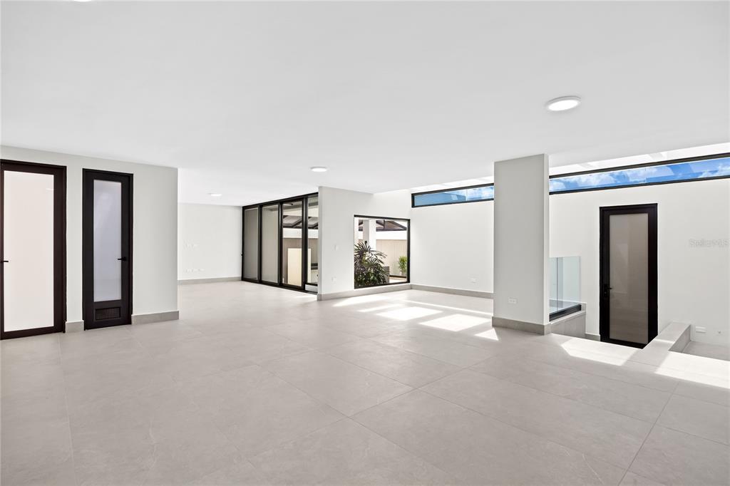 A minimalist, open-plan room features large light-gray floor tiles, white walls, and black-framed doors — La Villa de Torrimar REY JORGE 373, GUAYNABO, PR