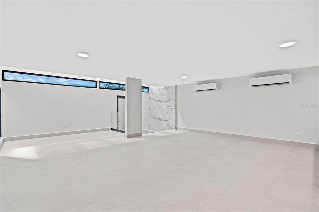 A minimalist room with light tile floors, white walls, two air conditioning units, and clerestory windows — La Villa de Torrimar REY JORGE 373, GUAYNABO, PR