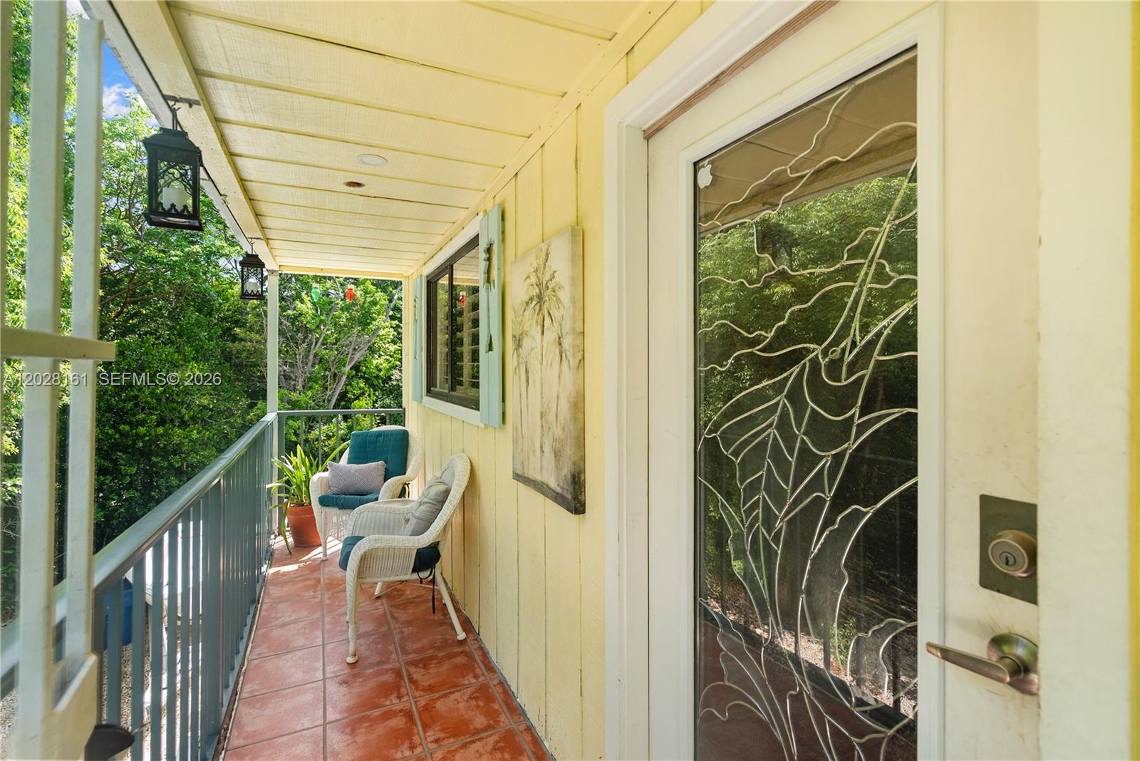 A yellow-sided balcony features a tiled floor, two wicker chairs, and a decorative glass door — 411 Mahogany Ave, Key Largo FL 33037, KEY LARGO, FL
