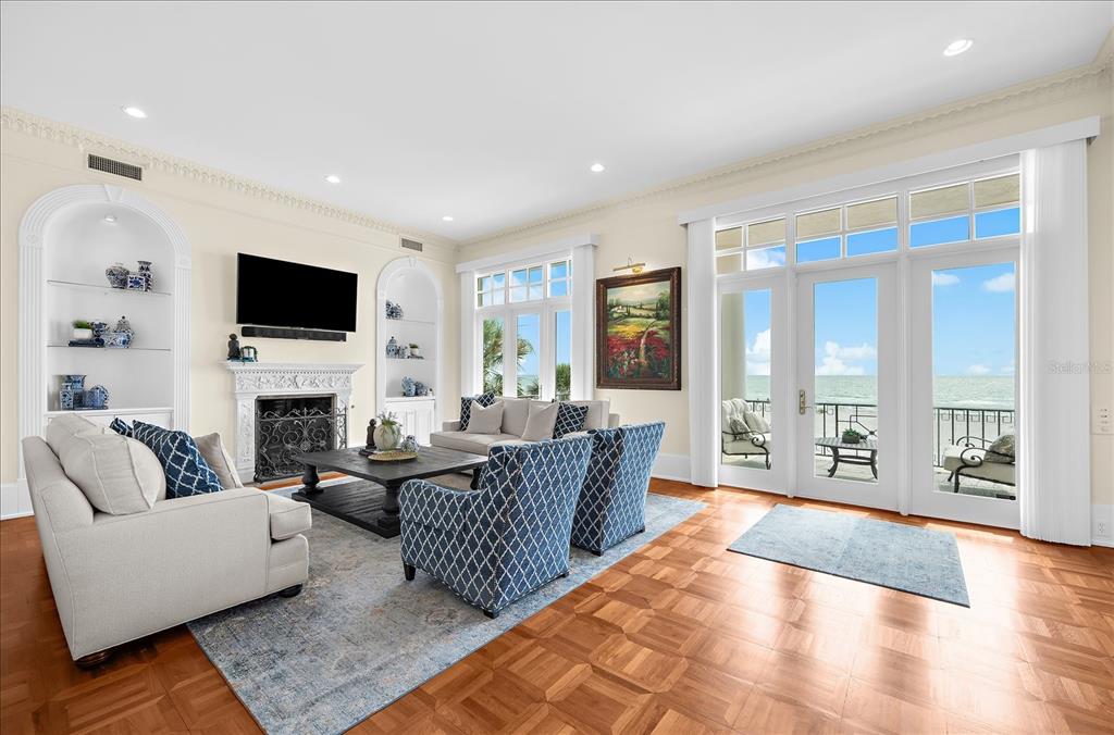 A living room features a fireplace, built-in shelving, blue patterned furniture, and ocean-view glass doors — 810 ELDORADO AVENUE, CLEARWATER BEACH, FL