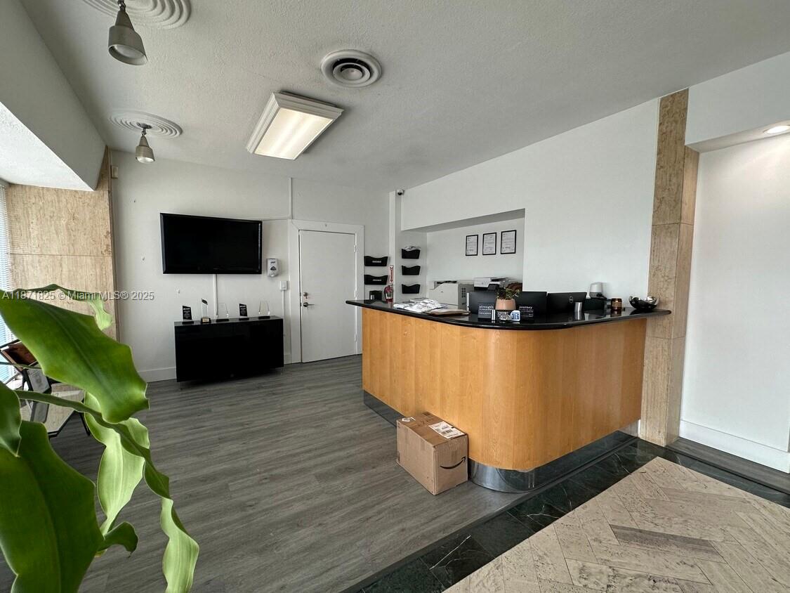 A reception area features a curved wooden desk, gray flooring, and a wall-mounted television — 2116 N Dixie Hwy, Hollywood FL 33020, HOLLYWOOD, FL