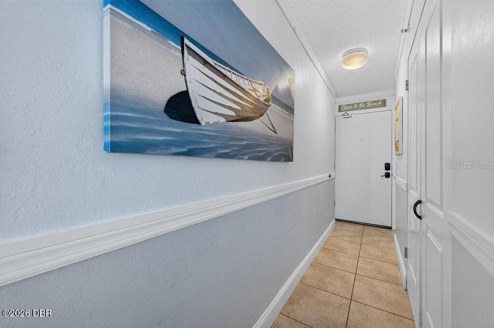 A hallway with light blue walls, tile flooring, a boat painting, and a white door — 701 S ATLANTIC AVENUE UNIT 502, DAYTONA BEACH, FL