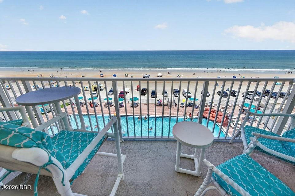 A balcony with two chairs and tables overlooks a swimming pool and the ocean beach — 701 S ATLANTIC AVENUE UNIT 502, DAYTONA BEACH, FL