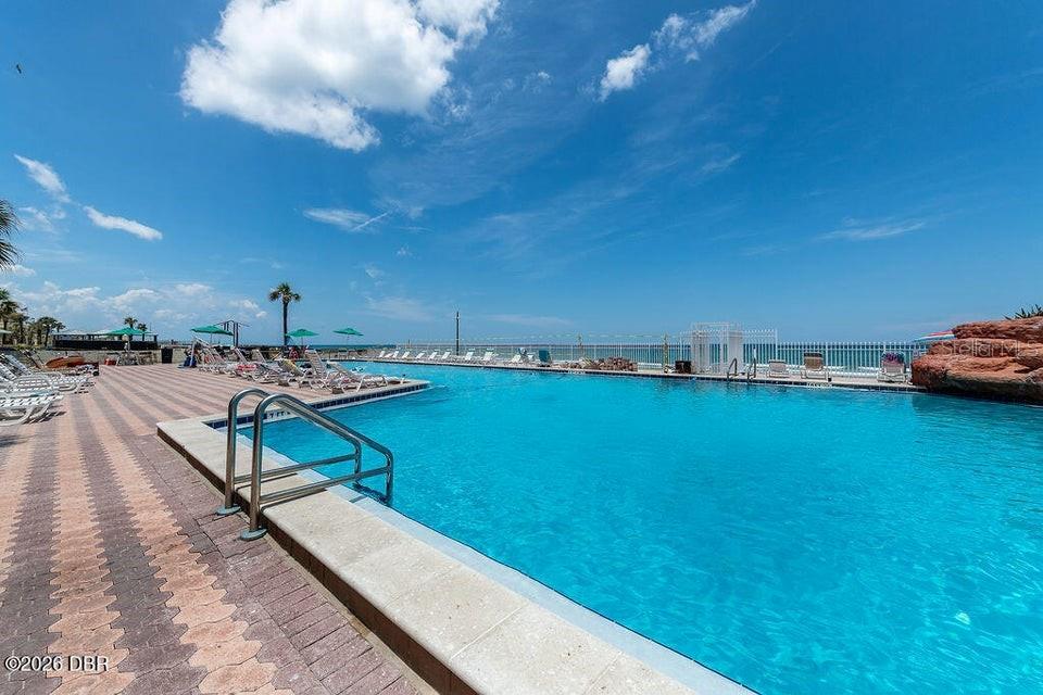 A large outdoor swimming pool overlooks the ocean with lounge chairs on a paved deck — 701 S ATLANTIC AVENUE UNIT 502, DAYTONA BEACH, FL
