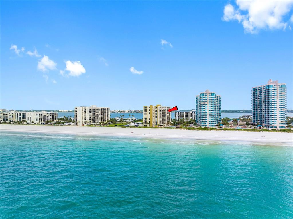 An aerial view shows several high-rise residential buildings situated along a sandy beach and ocean — 1480 GULF BOULEVARD UNIT 1011, CLEARWATER BEACH, FL
