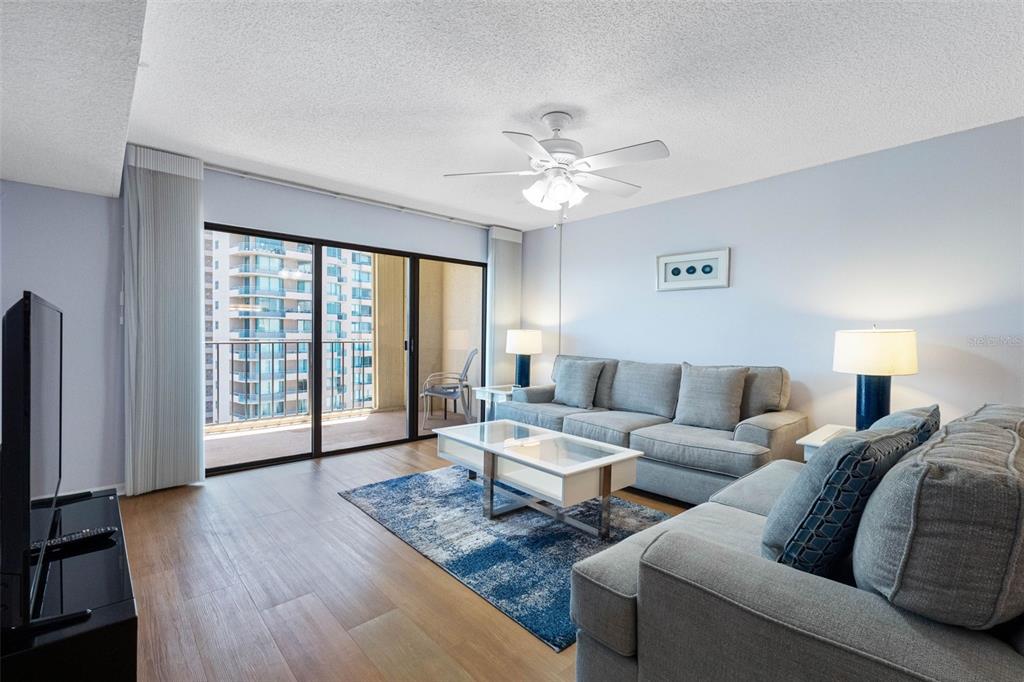 A living room features a grey sofa, a glass coffee table, and a balcony view — 1480 GULF BOULEVARD UNIT 1011, CLEARWATER BEACH, FL
