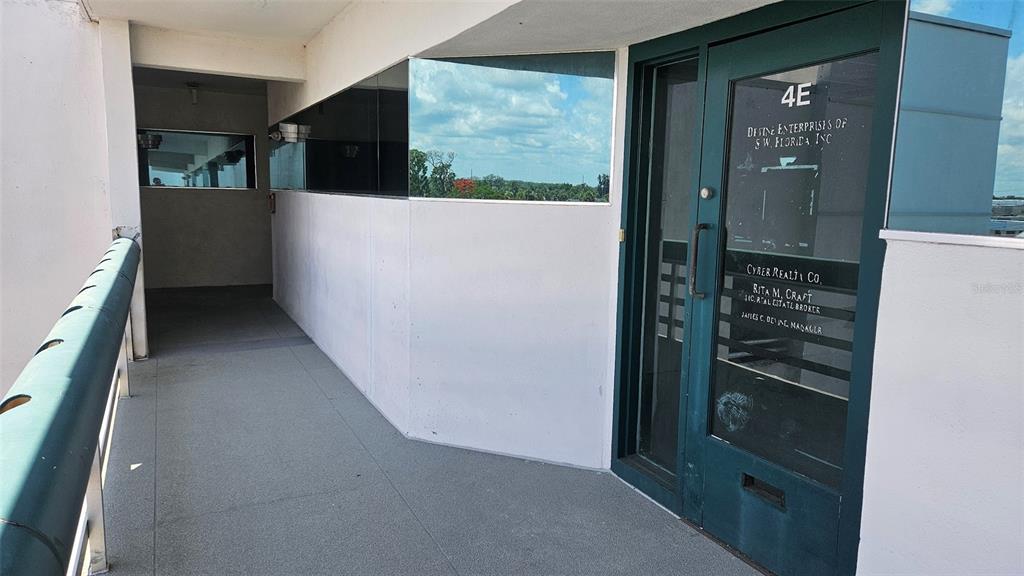 An exterior walkway leads to a glass office door labeled 4E on a building balcony — 1460 S MCCALL ROAD UNIT E4, ENGLEWOOD, FL