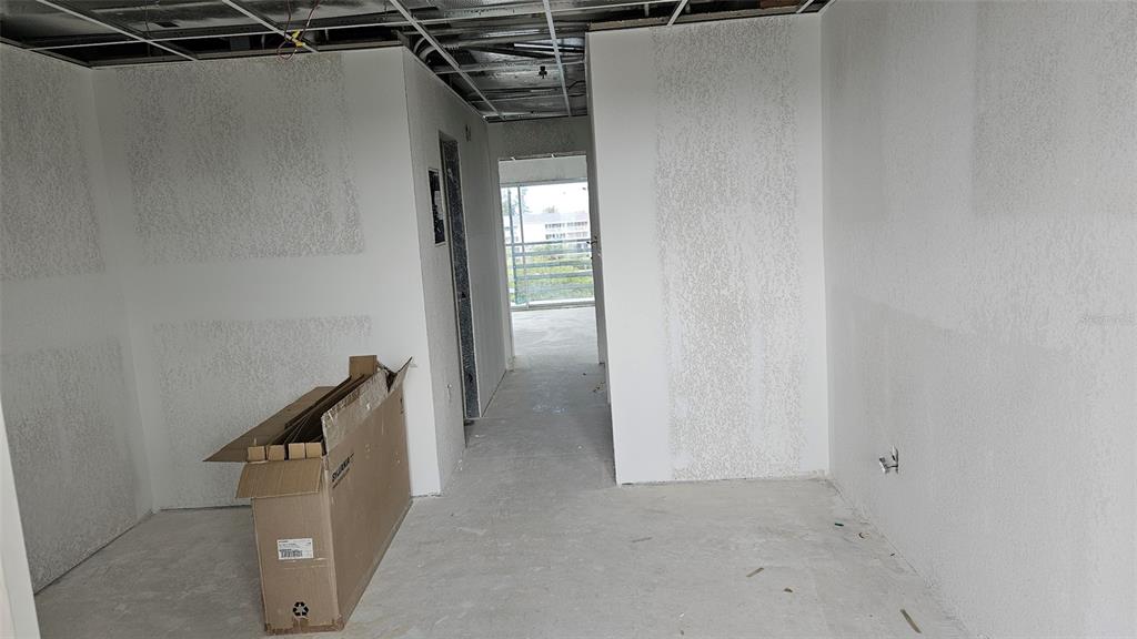 An unfinished interior room features white textured walls, exposed ceiling grid, and a cardboard box — 1460 S MCCALL ROAD UNIT E4, ENGLEWOOD, FL