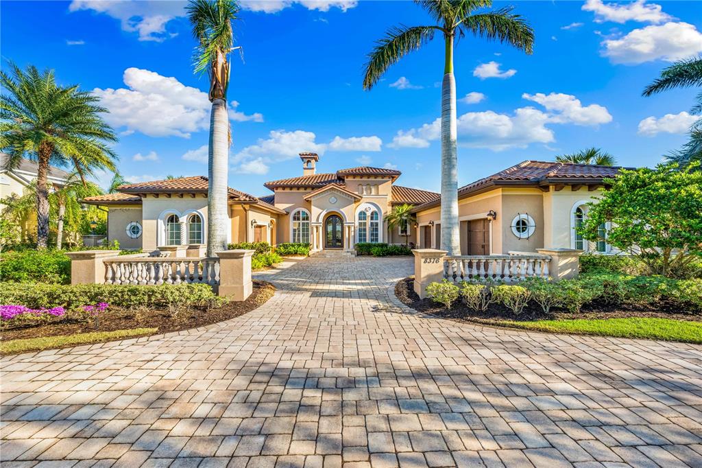 A paved driveway leads to the entrance of a single-story Mediterranean-style home with palm trees — 8376 CATAMARAN CIRCLE, LAKEWOOD RANCH, FL