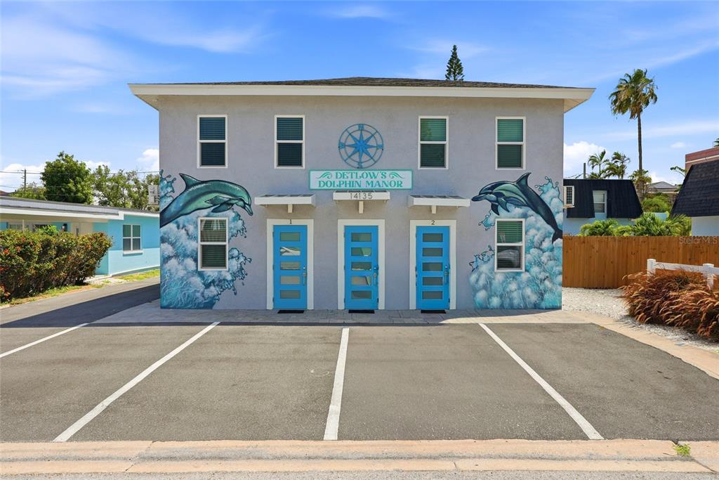 A two-story building with blue doors, dolphin murals, and a paved parking lot in front — 14135 PALM STREET, MADEIRA BEACH, FL