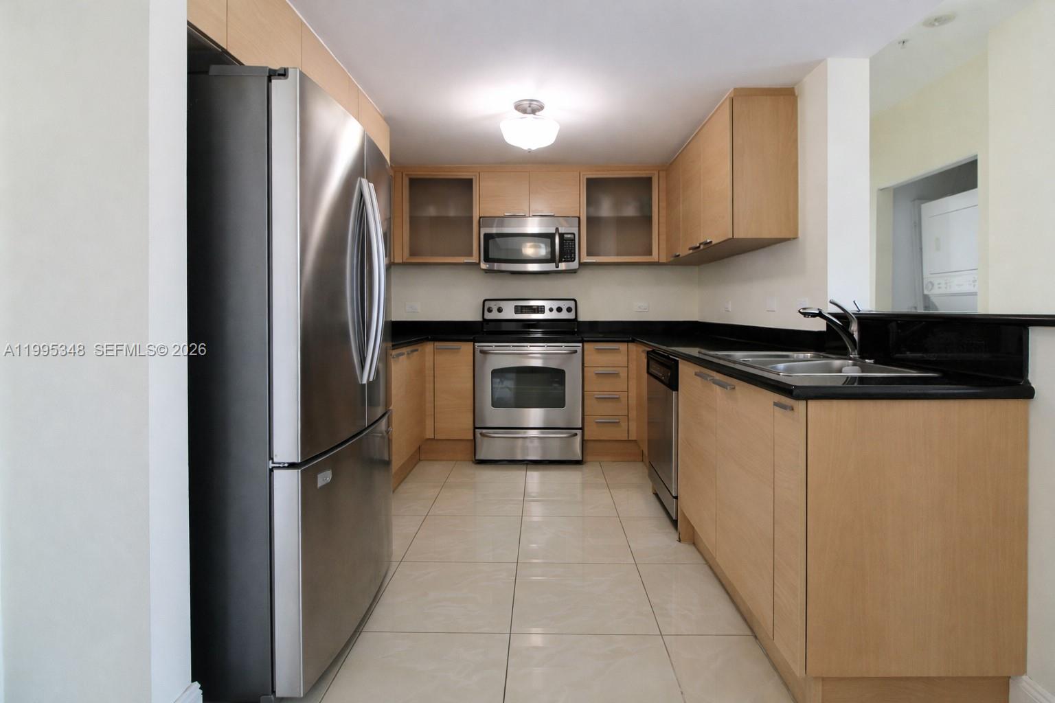 A galley kitchen features light wood cabinets, stainless steel appliances, and black countertops — 140 S Dixie Hwy # 1019, Hollywood FL 33020, HOLLYWOOD, FL