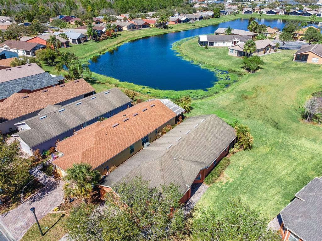 An aerial view shows suburban houses with brown roofs surrounding a small, blue retention pond — 524 MURANO DRIVE, POINCIANA, FL