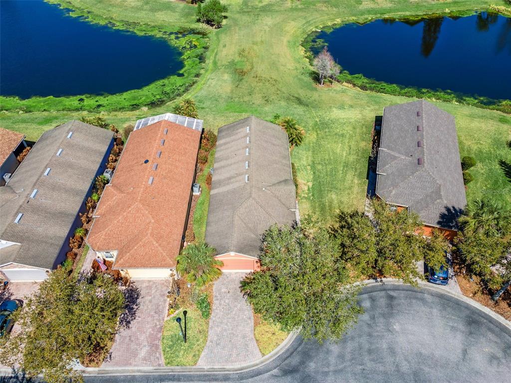 An aerial view shows three suburban houses with paved driveways situated near a golf course pond — 524 MURANO DRIVE, POINCIANA, FL
