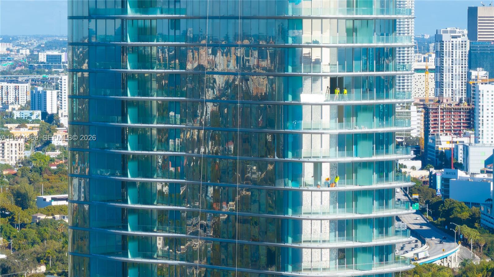 Exterior view of a modern glass skyscraper with workers visible on two balconies — 175 SE 25 Rd # 2802, Miami FL 33129, MIAMI, FL