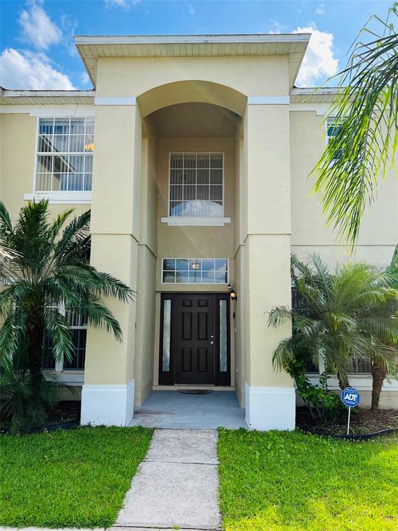 The exterior of a two-story house features a tan stucco facade, a dark front door, and palm trees — 5444 CREPE MYRTLE CIRCLE, KISSIMMEE, FL
