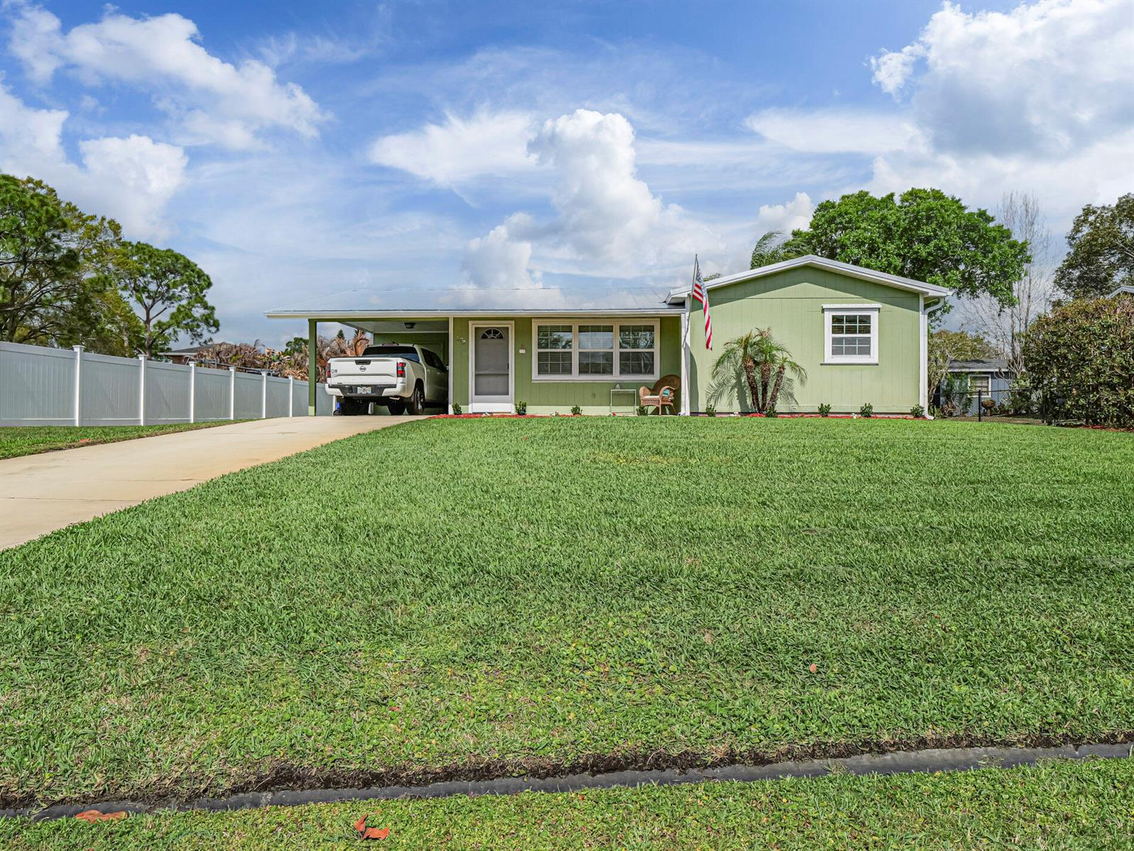 A light green single-story house with a carport, white fence, and a large front lawn — 573 Autumn Terrace, Sebastian FL 32958, SEBASTIAN, FL