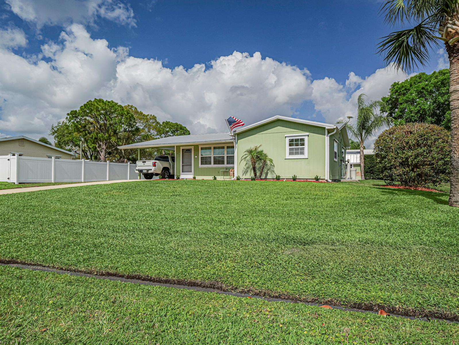 A light green single-story house with a carport, white fence, and a large front lawn — 573 Autumn Terrace, Sebastian FL 32958, SEBASTIAN, FL