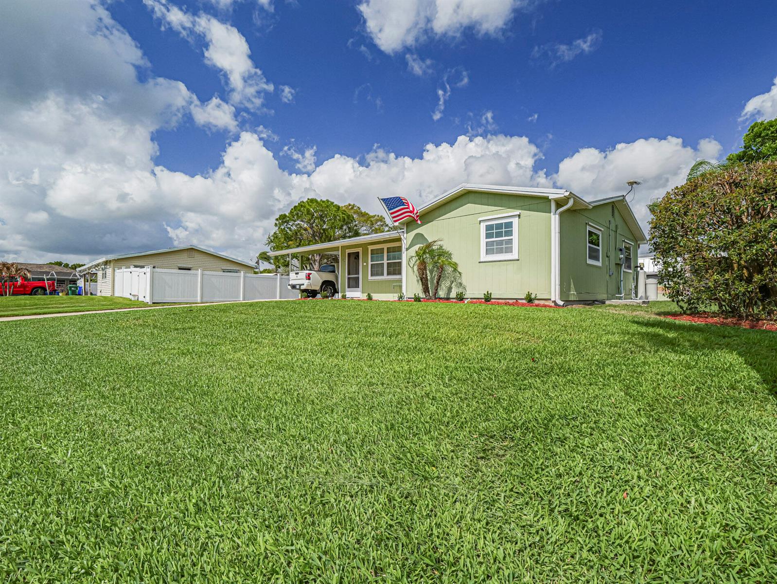 A light green single-story house with a white carport and an American flag — 573 Autumn Terrace, Sebastian FL 32958, SEBASTIAN, FL