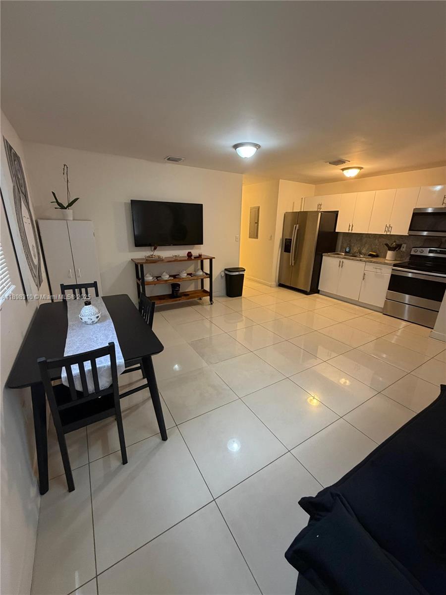 An open-concept kitchen and dining area features white cabinets, stainless steel appliances, and tiled floors — 1132 NW 38th St # 1132, Miami FL 33127, MIAMI, FL