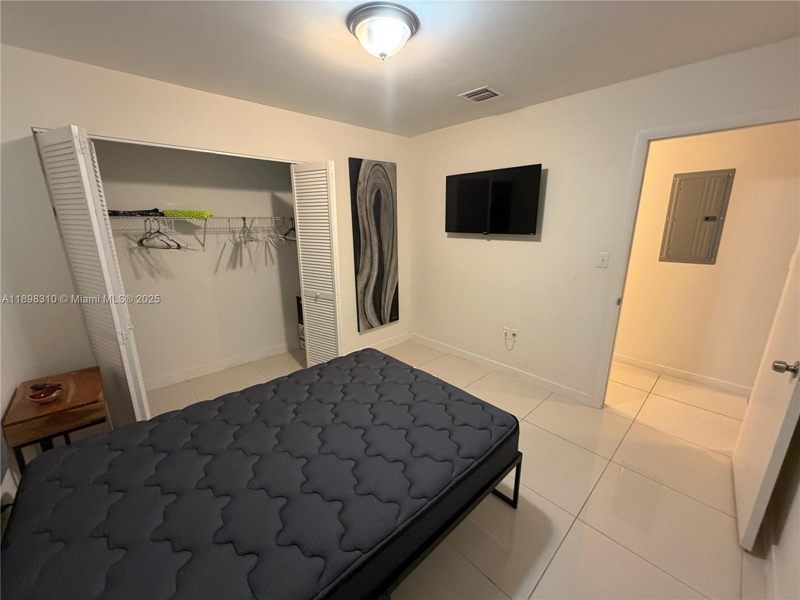 A bedroom features a dark mattress, a white closet, a wall-mounted television, and tiled floors — 1132 NW 38th St # 1132, Miami FL 33127, MIAMI, FL
