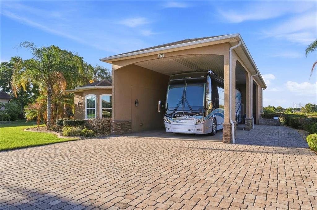 A large RV is parked under a covered carport attached to a residential home — 576 MEANDERING WAY, POLK CITY, FL