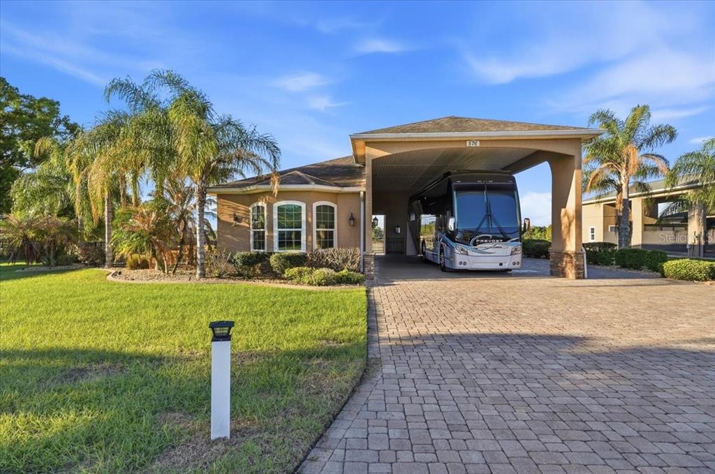A large motorhome is parked under the attached carport of a single-story stucco house — 576 MEANDERING WAY, POLK CITY, FL
