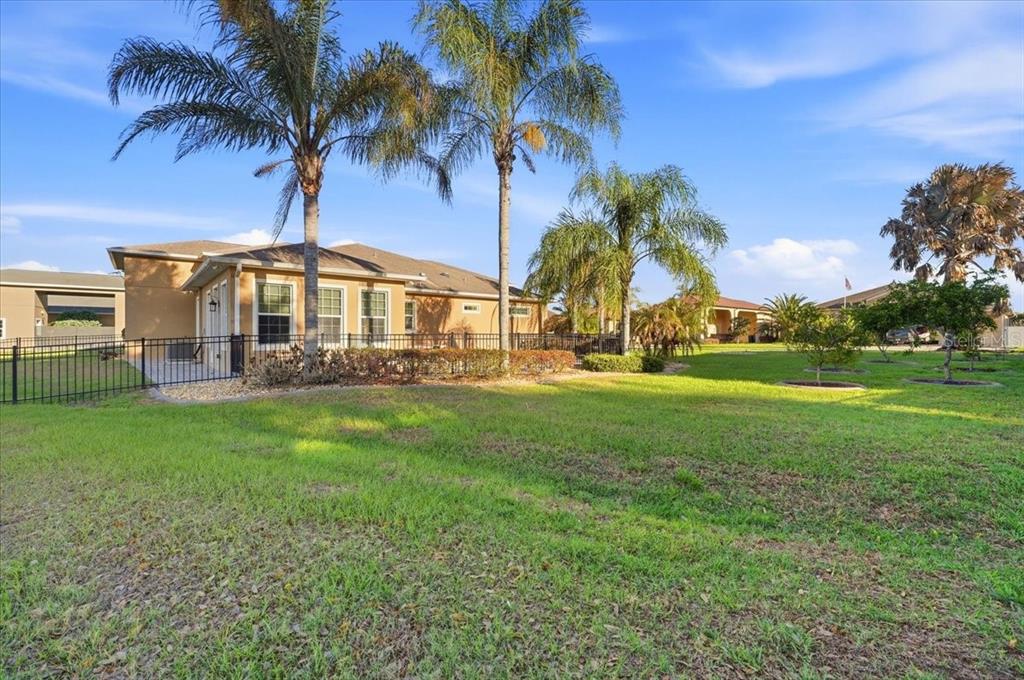 A backyard view of a tan house with palm trees and a black metal fence — 576 MEANDERING WAY, POLK CITY, FL