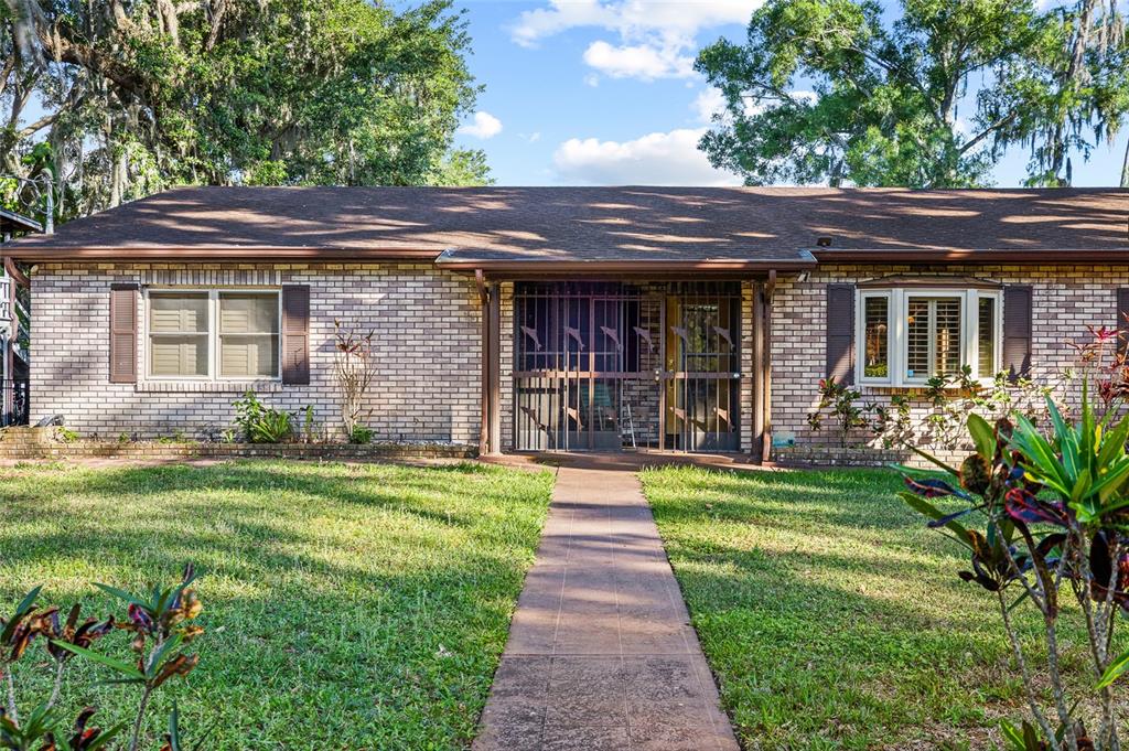 A single-story brick house with a front walkway and a metal security screen door — 16025 CHASTAIN ROAD, ODESSA, FL