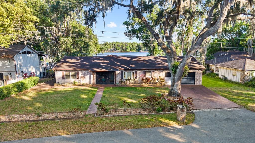 An exterior view of a single-story brick house with a large tree and lake view — 16025 CHASTAIN ROAD, ODESSA, FL