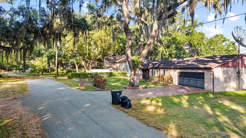 A single-story brick house with a garage sits on a lot shaded by large trees — 16025 CHASTAIN ROAD, ODESSA, FL