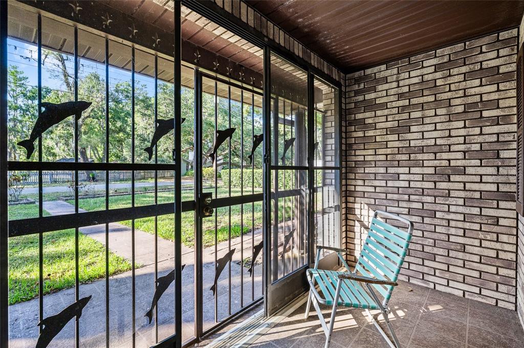 A covered porch features a brick wall, a folding chair, and a metal screen door — 16025 CHASTAIN ROAD, ODESSA, FL