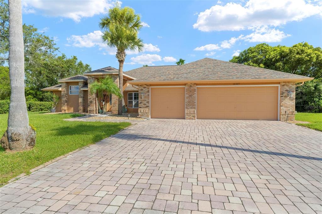 A single-story brick house features a paved driveway, a three-car garage, and a palm tree — 14207 CORNEWALL LANE, SPRING HILL, FL