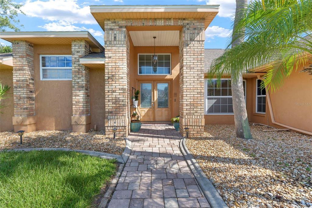 A brick-accented entryway features a stone walkway leading to double front doors — 14207 CORNEWALL LANE, SPRING HILL, FL