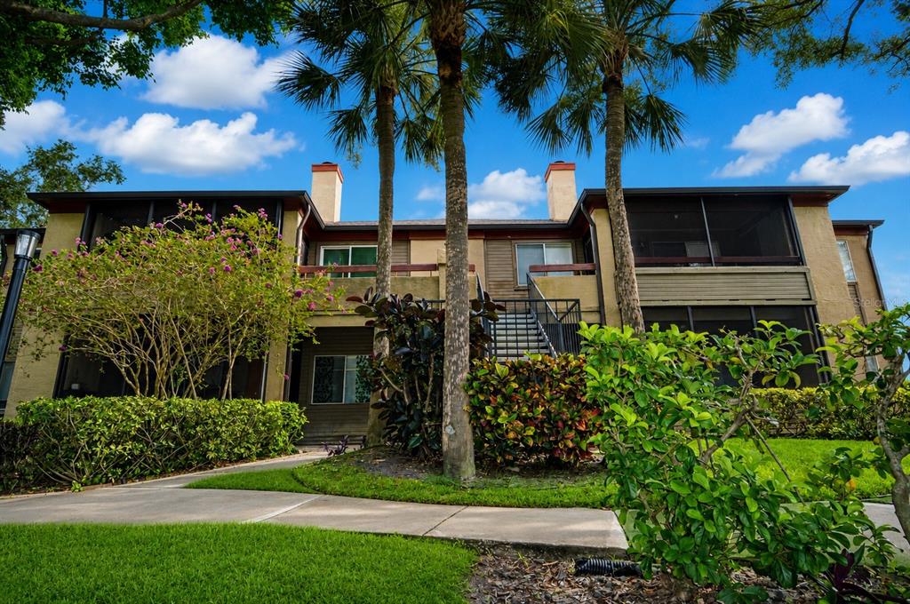 A two-story apartment building exterior with palm trees, screened balconies, and a central staircase — 10263 GANDY BOULEVARD N UNIT 2407, ST PETERSBURG, FL
