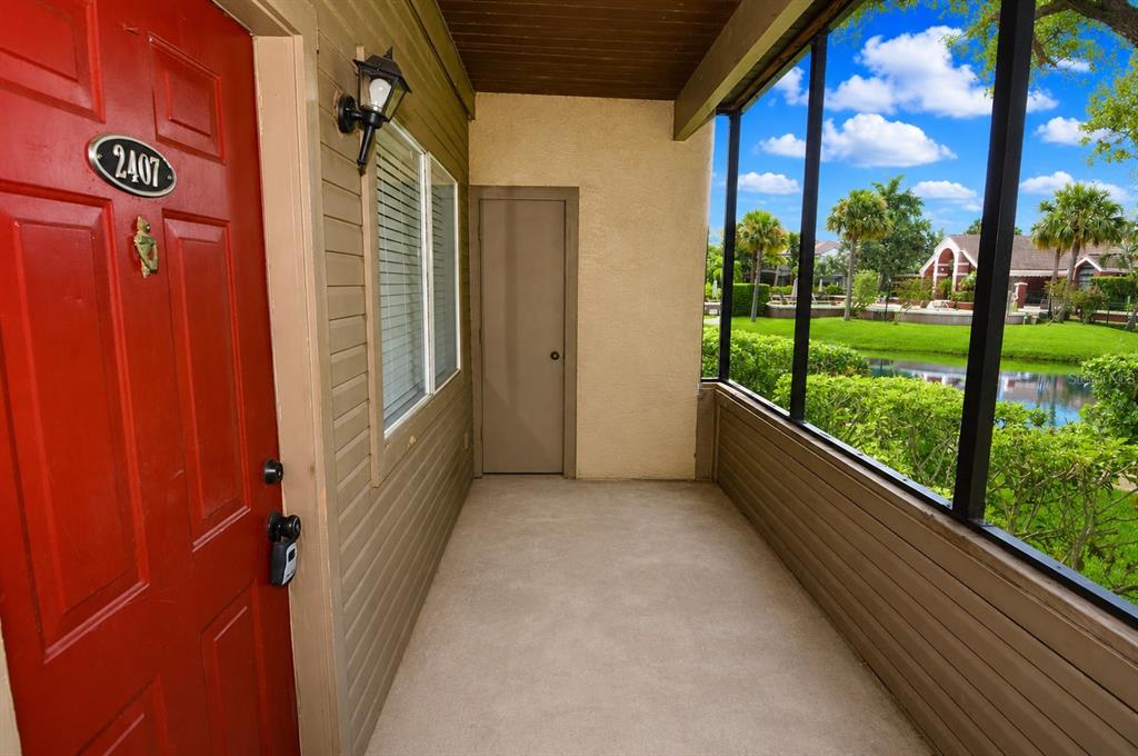 A red front door opens onto a screened-in porch overlooking a pond and palm trees — 10263 GANDY BOULEVARD N UNIT 2407, ST PETERSBURG, FL