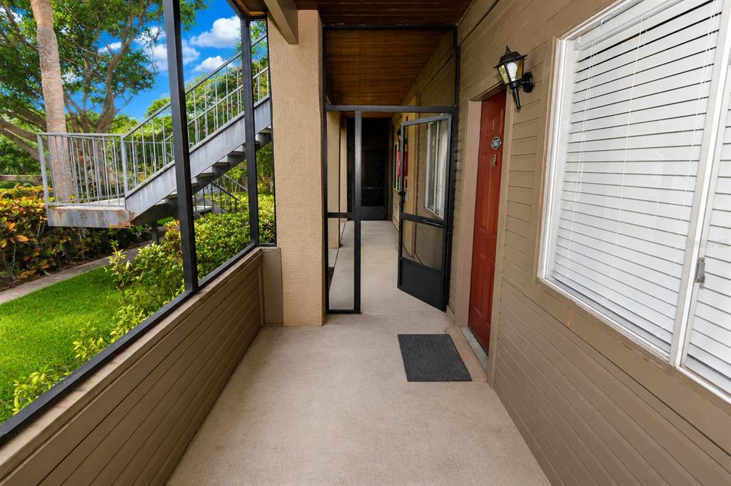 A covered exterior walkway leads to a red front door with a screen door — 10263 GANDY BOULEVARD N UNIT 2407, ST PETERSBURG, FL