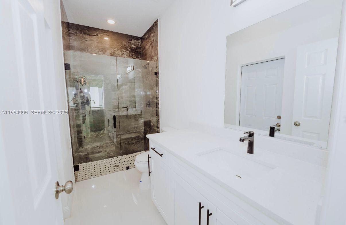 A bathroom features a white vanity, a glass-enclosed shower with marble tile, and white flooring — 4405 E 7th, Lehigh Acres FL 33972, LEHIGH ACRES, FL